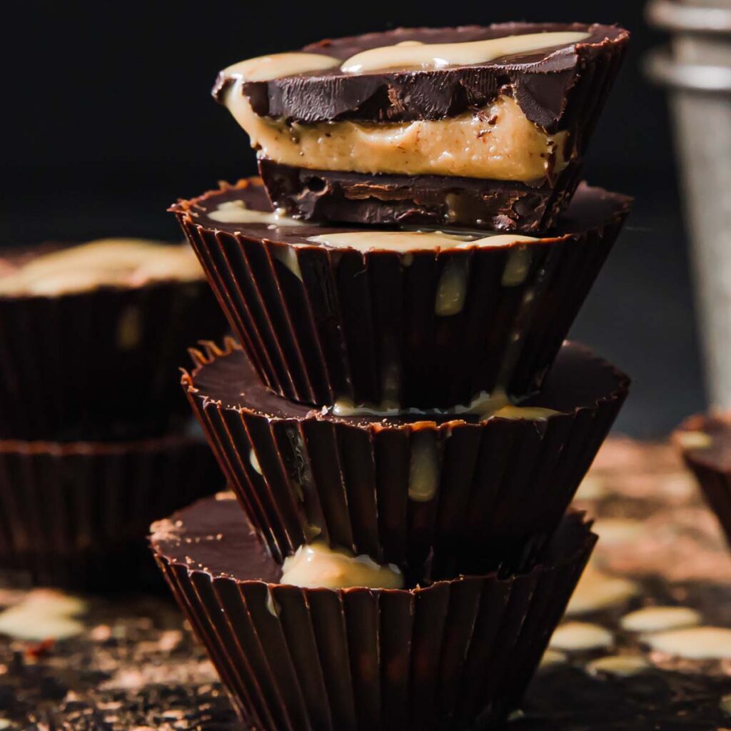 a stack of 4 keto peanut butter cups, the top one is halved showing the peanut centre
