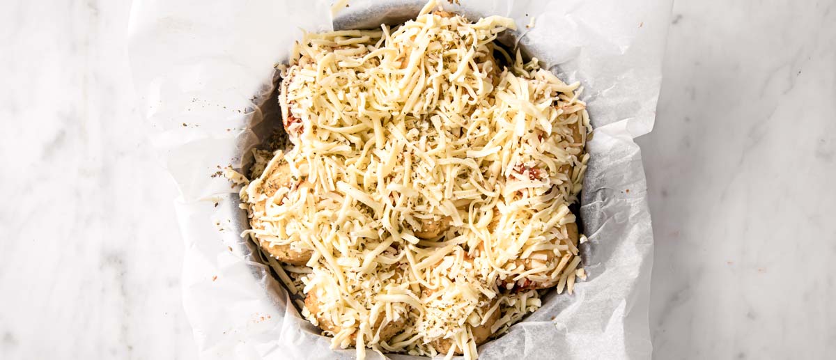 unbaked rolls in a pan lined with parchment paper topped with grated cheese