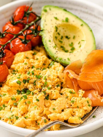 a plate with scrambled eggs, smoked salmon, avocado and tomatoes