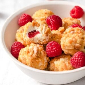 keto raspberry cheesecake bites in a bowl, one is halved showing the raspberry in the centre