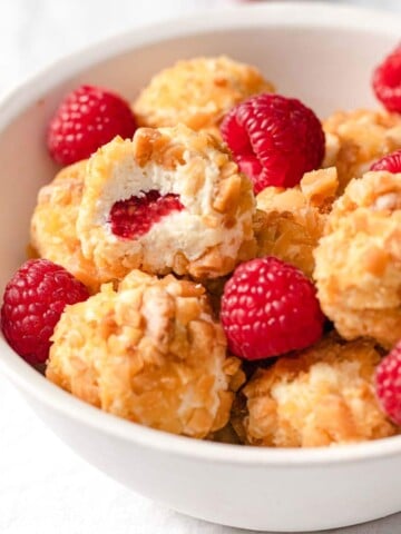 keto raspberry cheesecake bites in a bowl, one is halved showing the raspberry in the centre