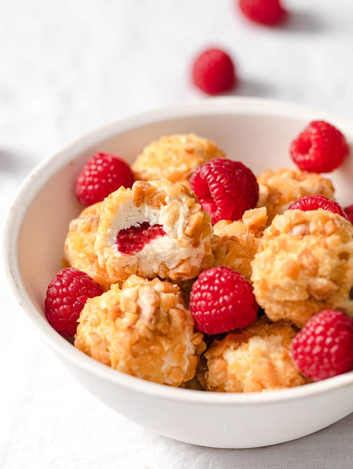 a bitten cheesecake bite in a bowl showing the raspberry in the centre