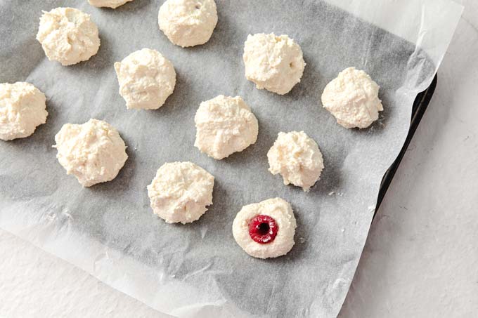 cheesecake balls on parchment paper showing a raspberry pressed into the centres