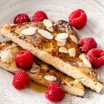 french toast slices on a plate with almonds and raspberries