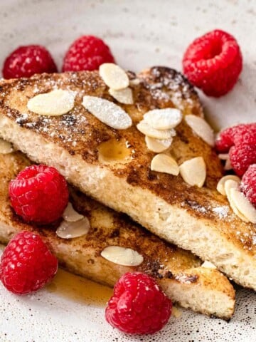 french toast slices on a plate with almonds and raspberries