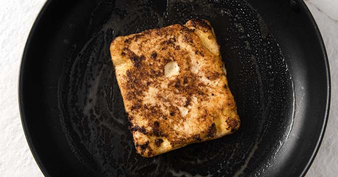 a slice of toast coated in egg and brown sweetener in a frying pan