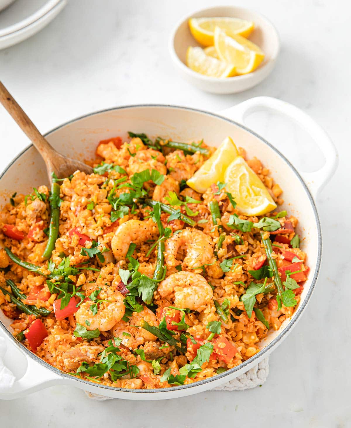 a pan with cauliflower paella with prawns and chorizo and beans topped with parsley and lemon slices