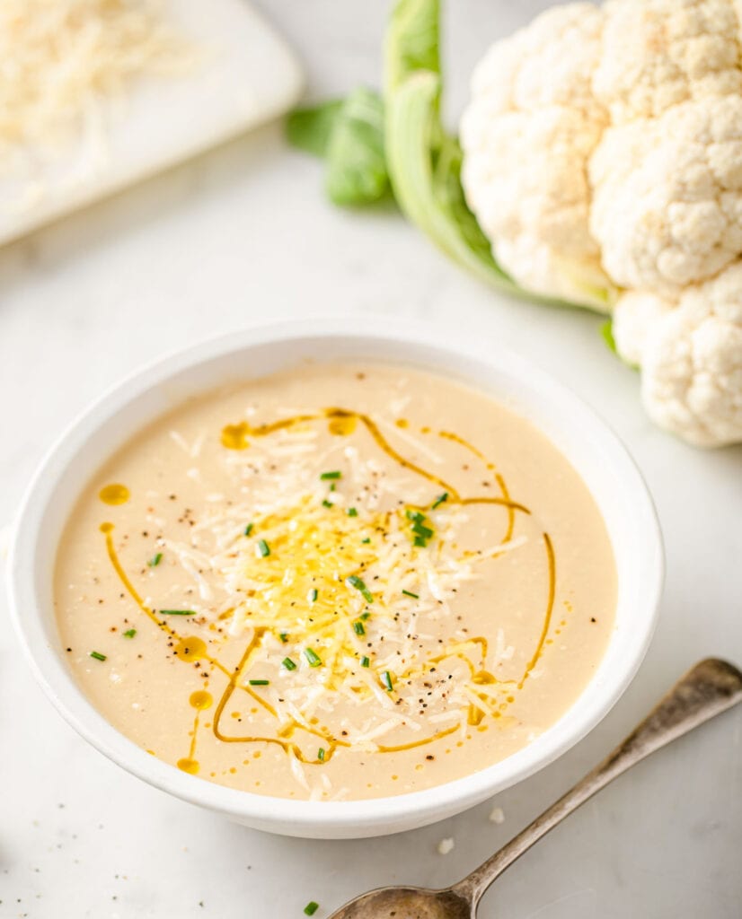 a bowl of roasted cauliflower soup drizzled with olive oil and topped with cheese and chives