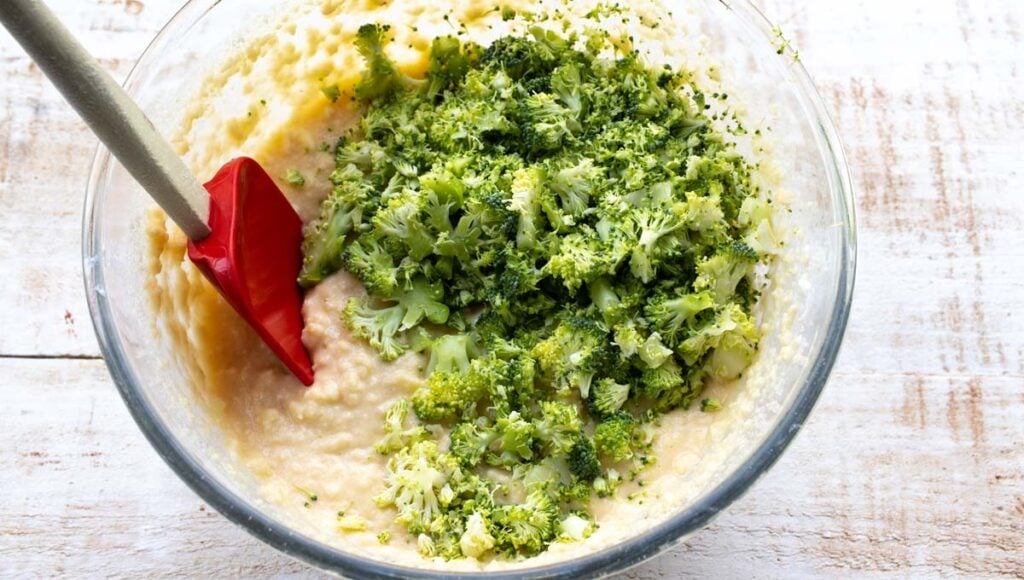 cheese muffin batter and chopped broccoli in a bowl and a spatula