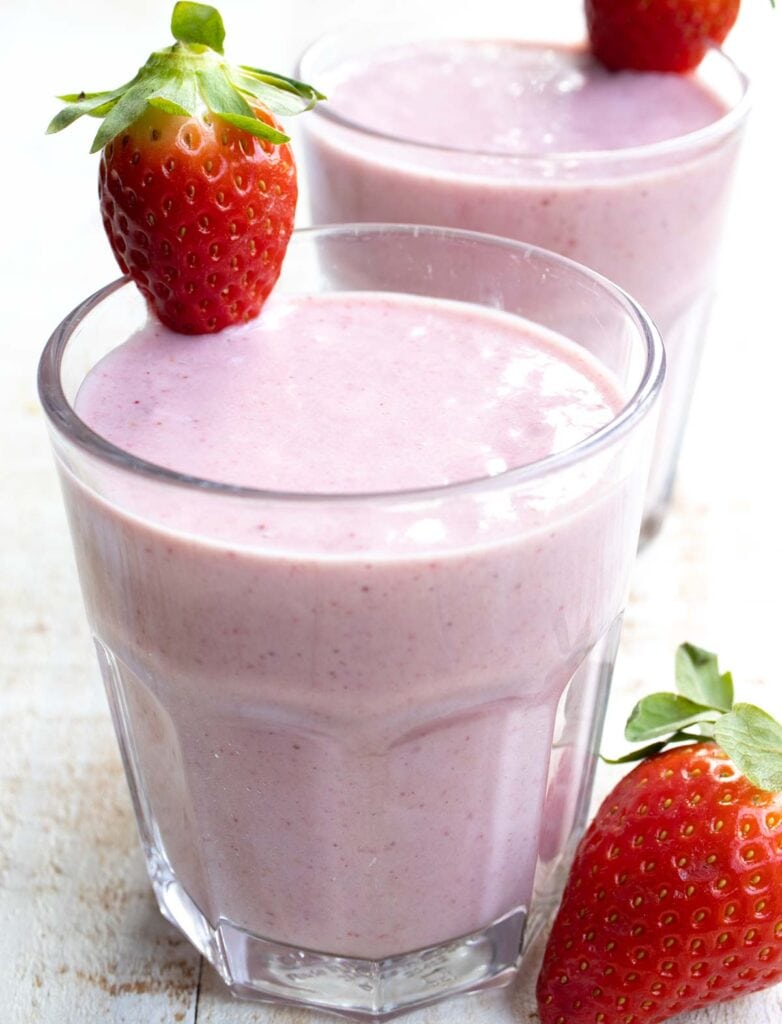 two glasses of strawberry smoothie decorated with fresh strawberries