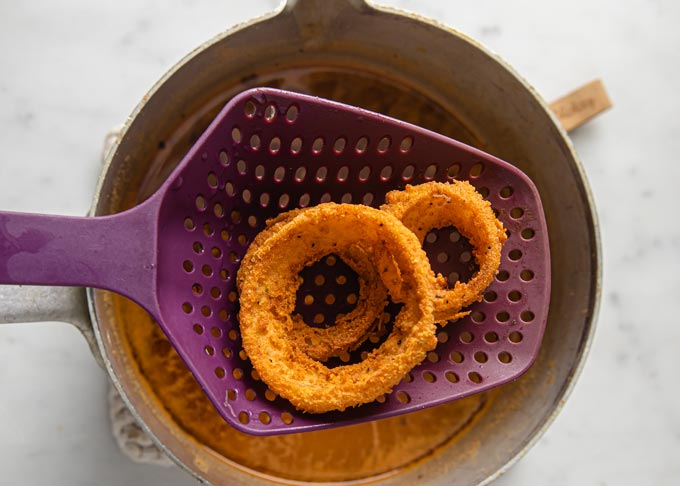removing onion rings from the frying pan with a slotted spoon