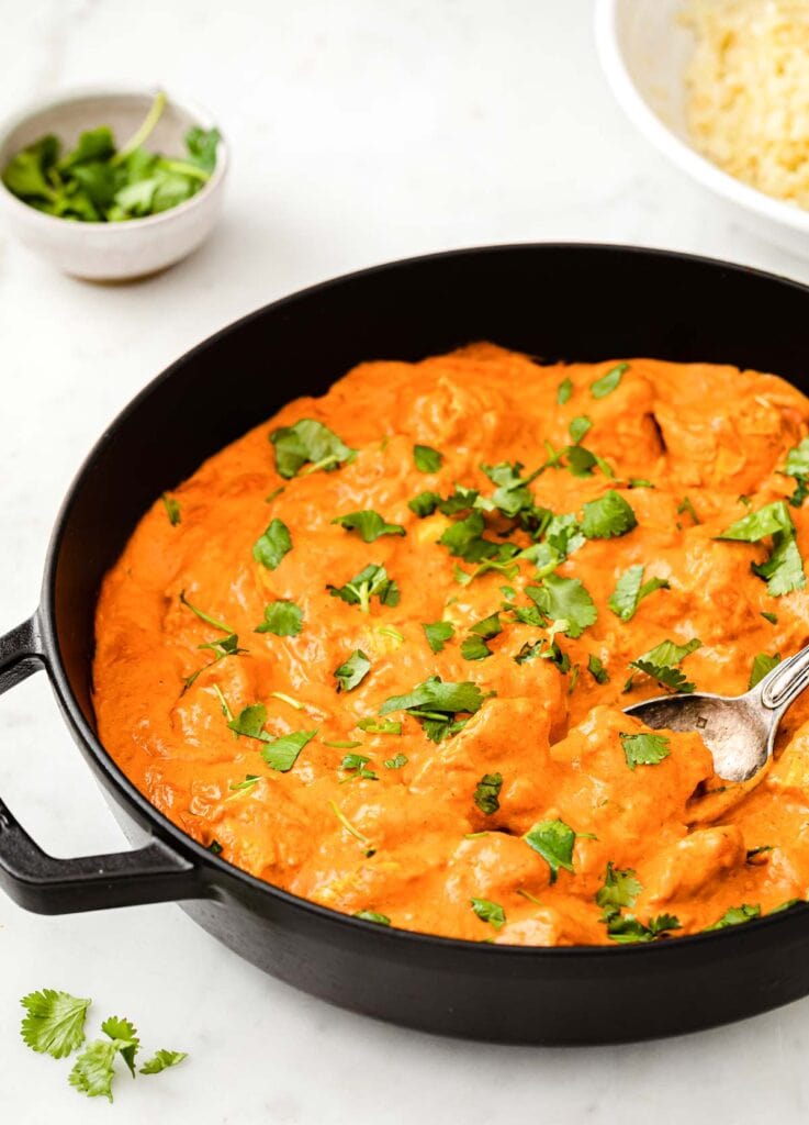 a cast iron pan with chicken tikka masala sprinkled with coriander