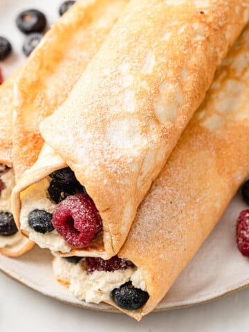 protein crepes on a plate, rolled up and filled with cream and berries