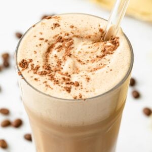 a frothy keto coffee smoothie with a glass straw and topped with cocoa powder