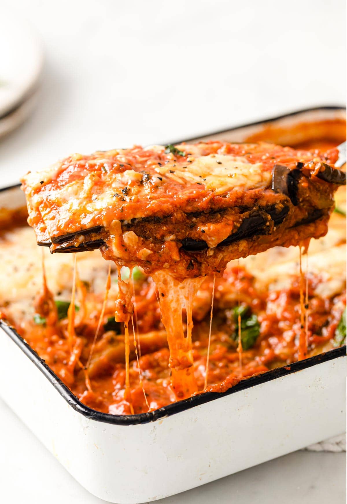 Spatula lifting a portion of baked aubergine parmigiana from a casserole dish
