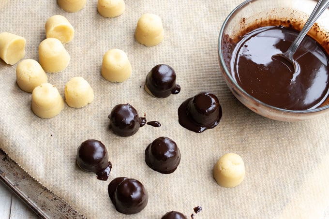 dipping marzipan balls into a bowl with melted chocolate