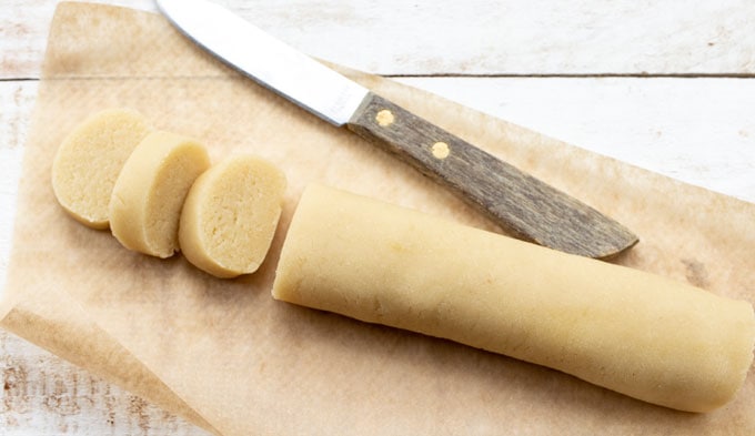 A log of marzipan sliced and a knife.