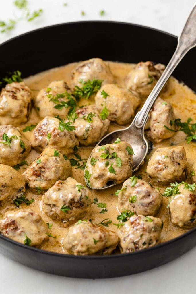 Low carb Swedish meatballs in a pan topped with fresh parsley and a spoon