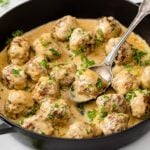 a frying pan filled with meatballs in a creamy sauce topped with chopped parsley
