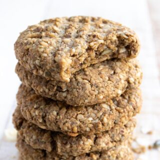 a stack of seeded keto breakfast cookies with a criss cross pattern on the tops, the top cookie has been bitten into