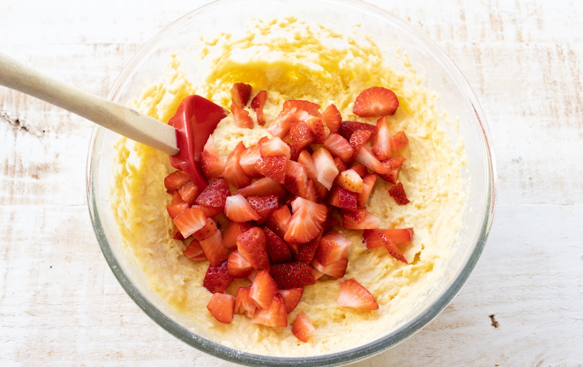 batter in a bowl with chopped strawberries and a spatula