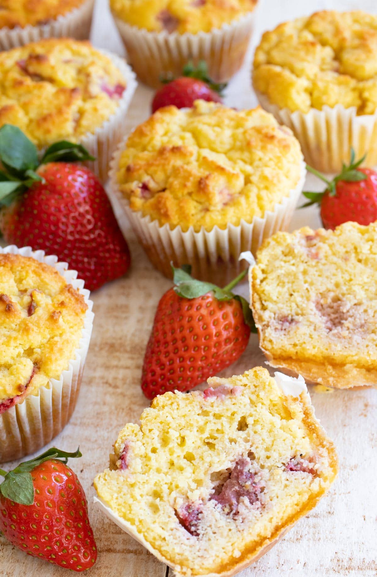 a halved strawberry muffin o a table showing the inside, surrounded by strawberries and more muffins in the background