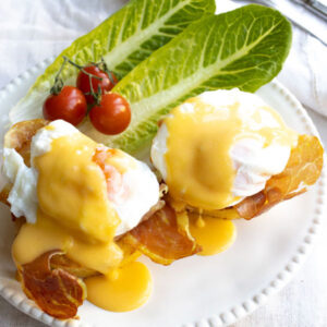 Eggs benedict with hollandaise sauce o a plate with salad garnish