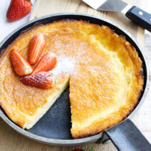 A dutch baby pancake topped with strawberry slices in a frying pan