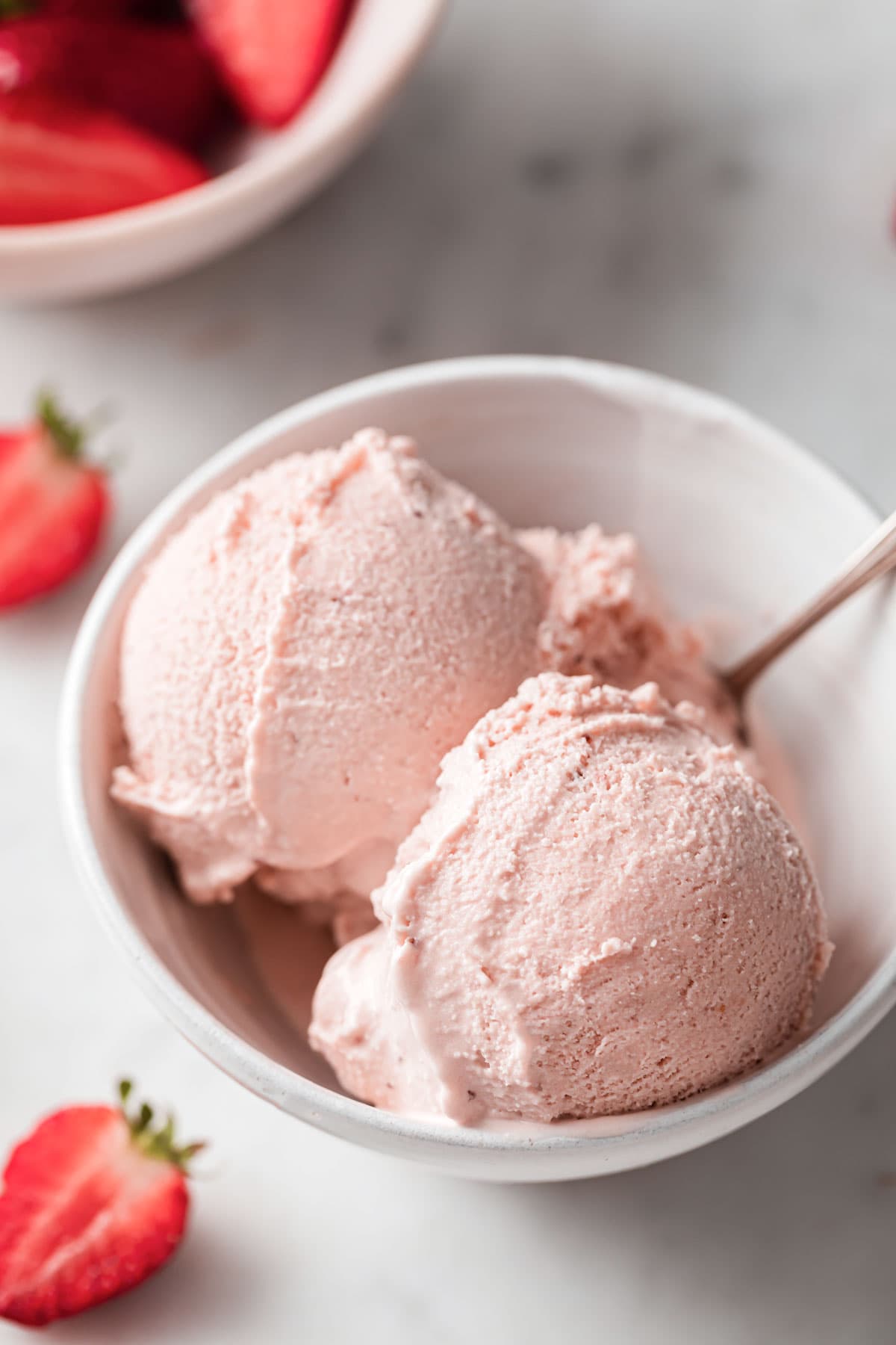 two scoops of strawberry ice cream in a bowl with a spoon