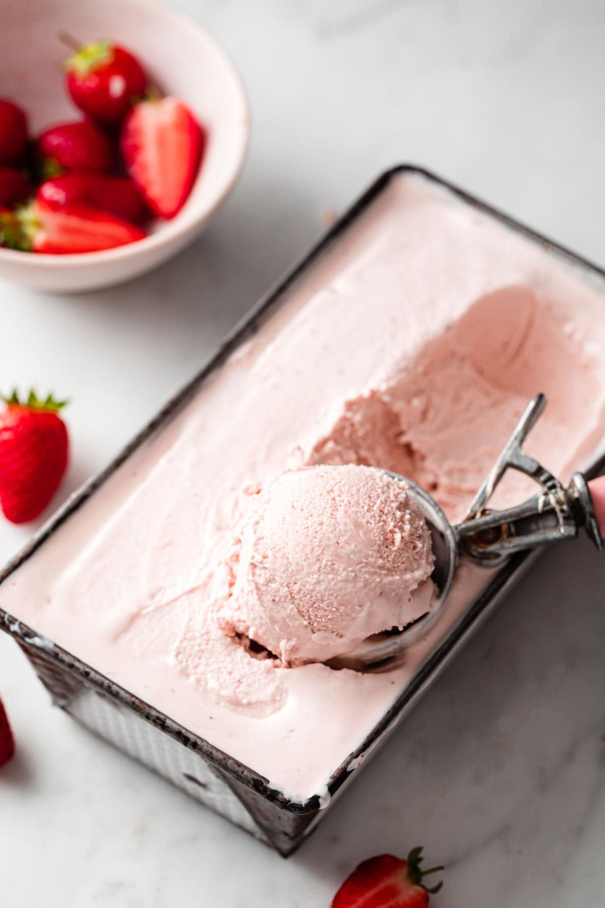 scooping low carb strawberry ice cream out of a container