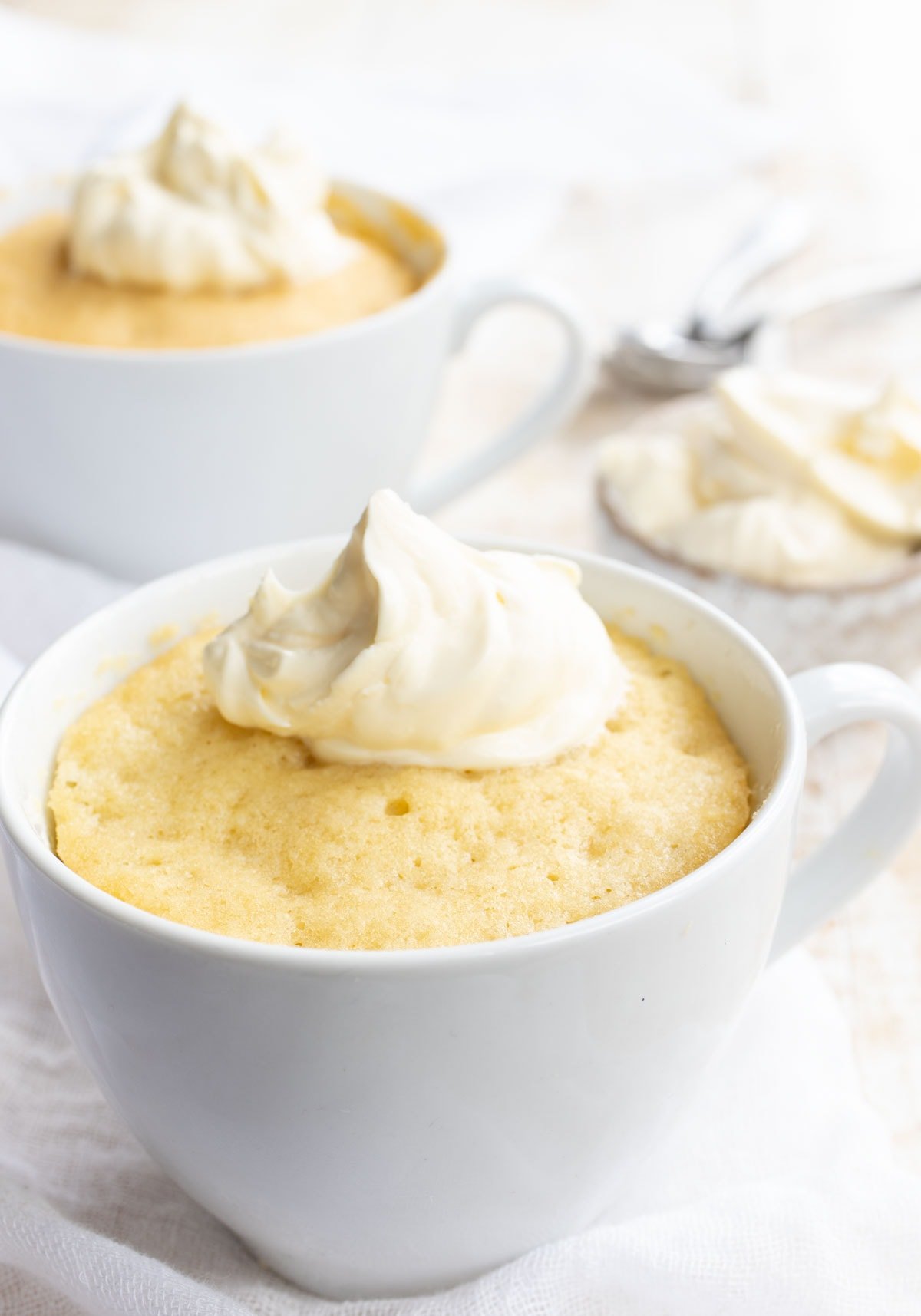 two mugs with vanilla mug cakes topped with whipped cream