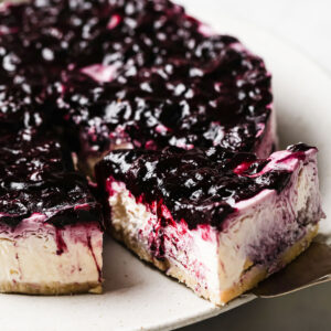 taking a slice of blueberry topped no bake cheesecake from a cake