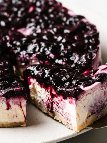 taking a slice of blueberry topped no bake cheesecake from a cake