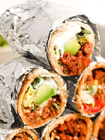a stack of keto beef burritos packed in aluminium foil and sliced in half