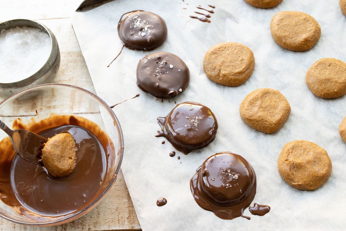 dipping peanut butter cookies into melted chocolate and chocolate dipped cookies on parchment paper