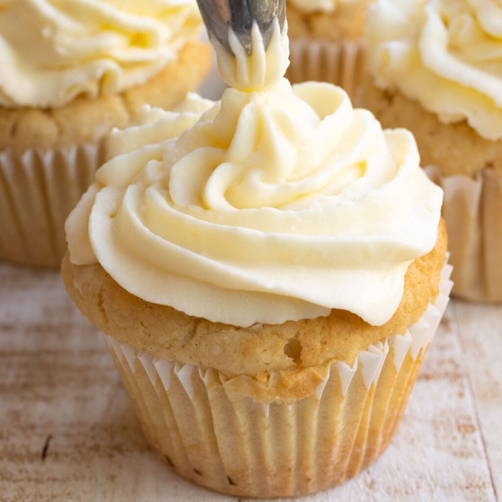 topping off a keto vanilla cupcake with cream cheese frosting