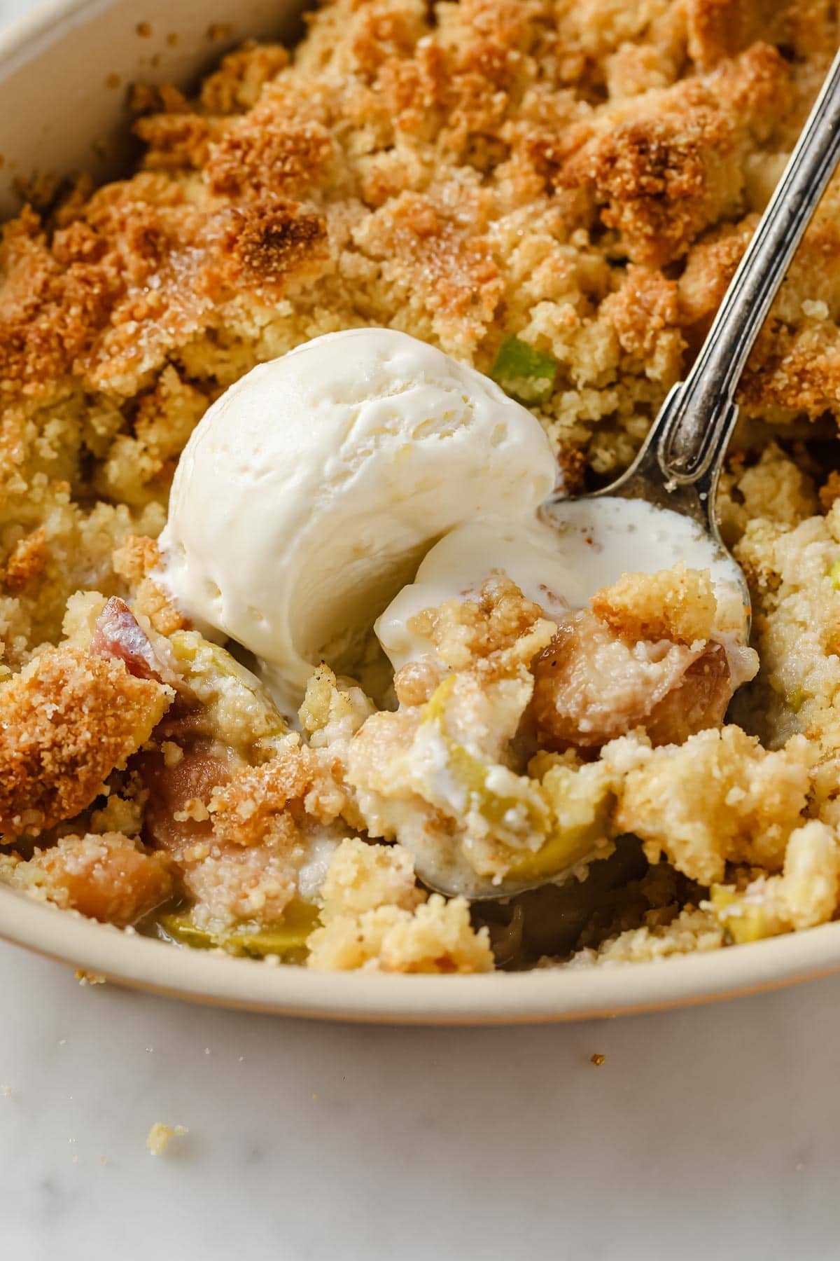 a peach crumble in a casserole dish and a scoop if ice cream