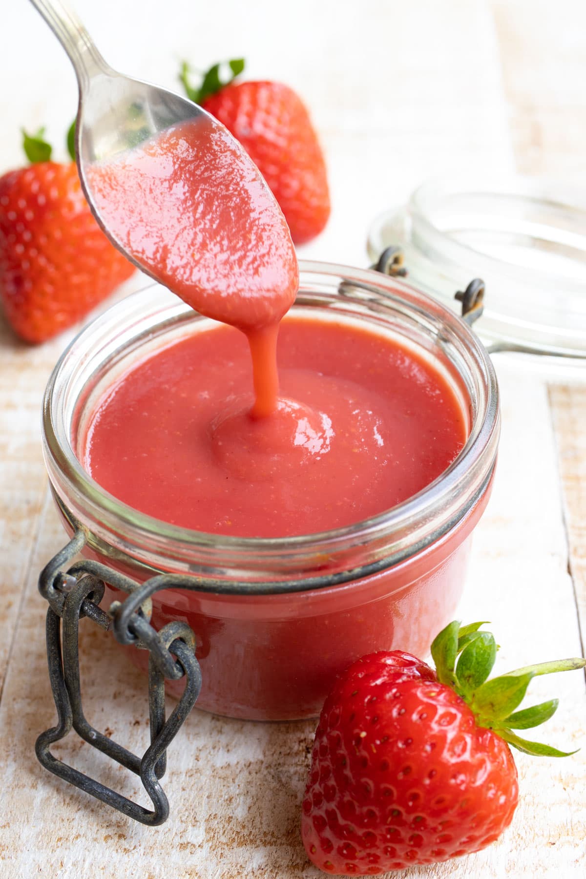 a glass jar with strawberry sauce and a spoon