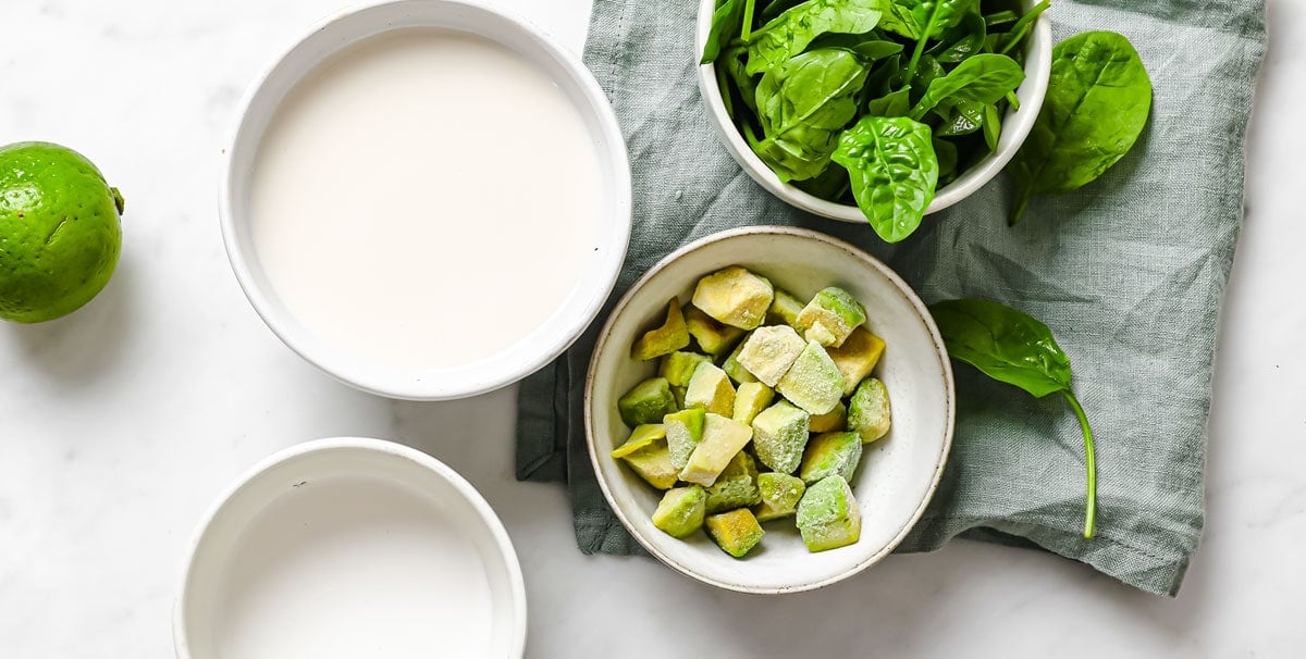 cubed avocado, spinach leaves, lime and nut milks in bowls