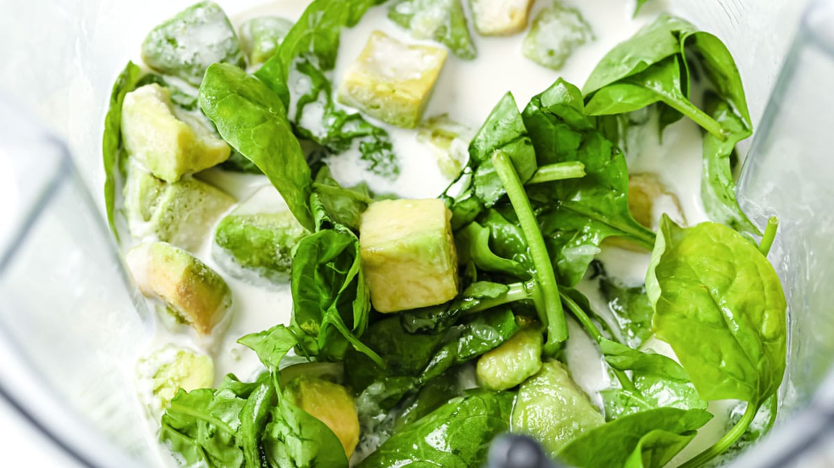 spinach, avocado cubes and nut milk in a blender cup