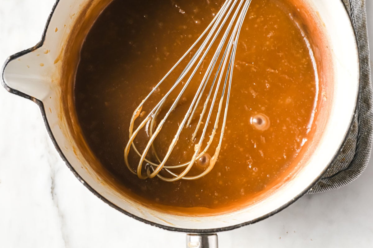 a balloon whisk stirring caramel sauce in a saucepan