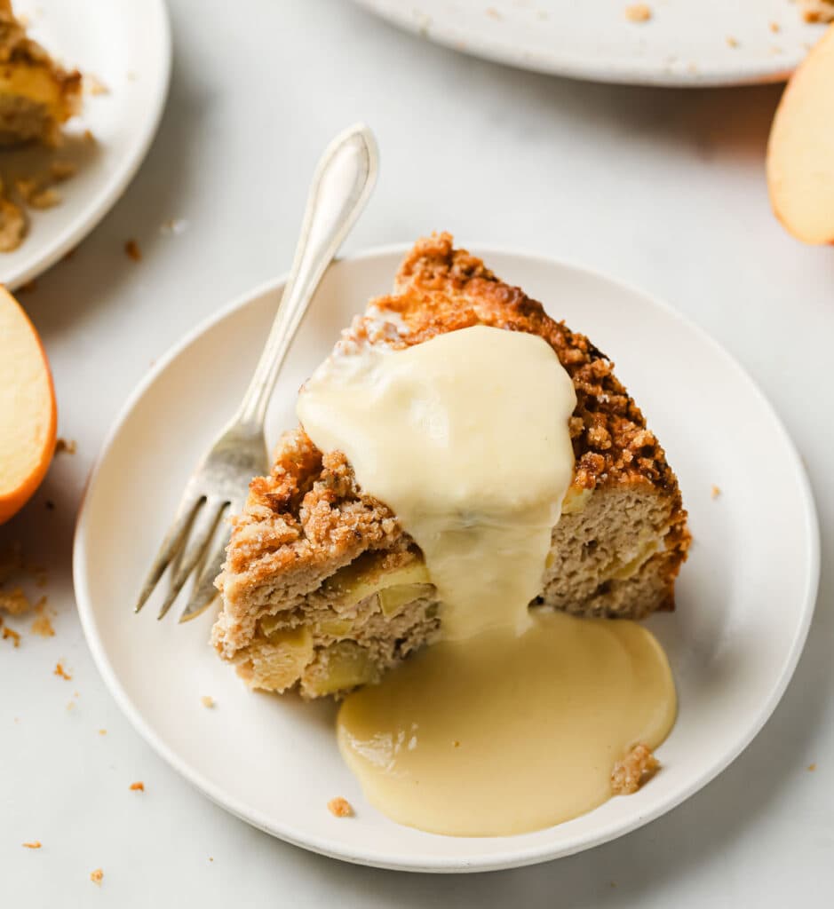 a slice of apple cake on a plate with a fork and vanilla custard