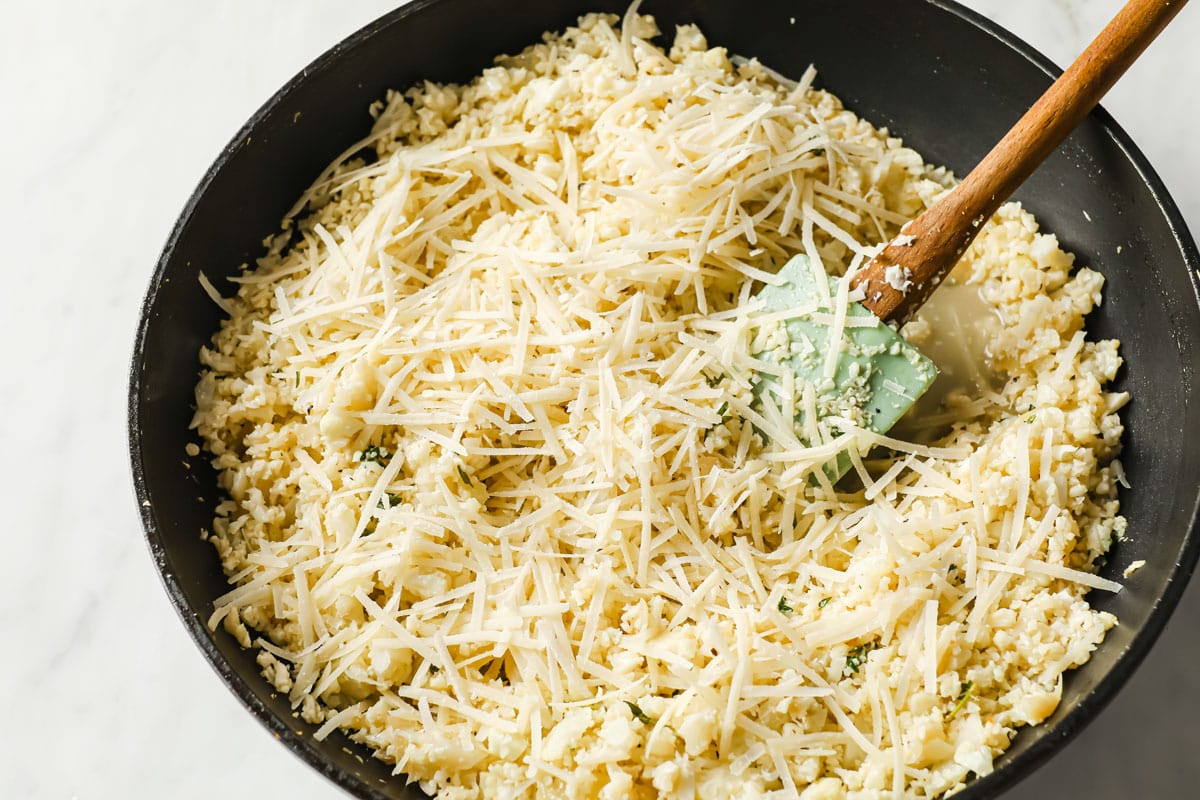 adding grated parmesan to cauliflower risotto in a pan