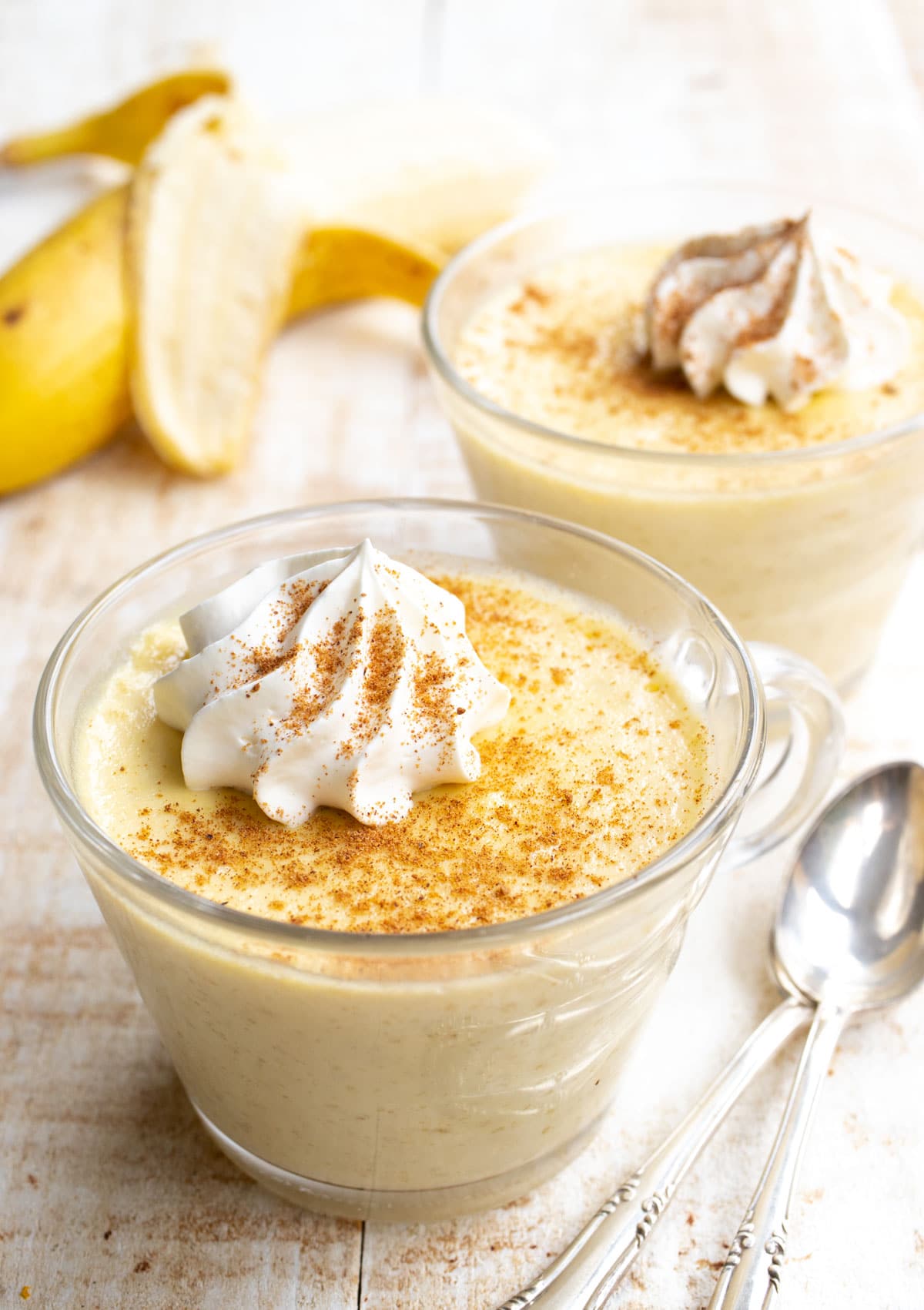 two dessert cups of low carb banana pudding with spoons and a banana
