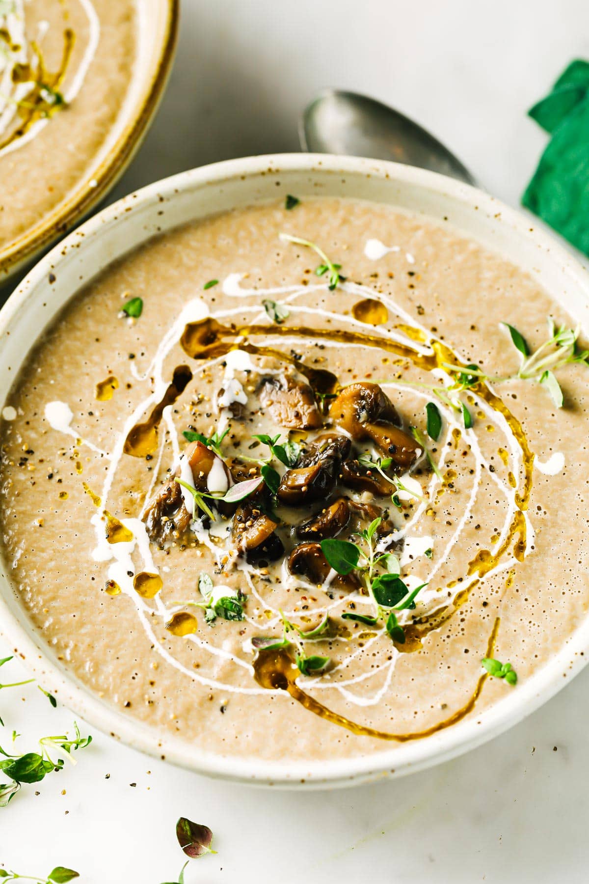Closeup of a soup topped with olive oil and cream swirls and mushrooms.
