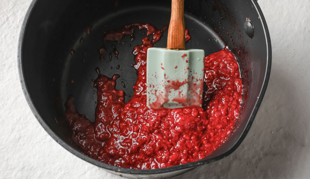 Raspberry sauce in a saucepan and a spatula. 