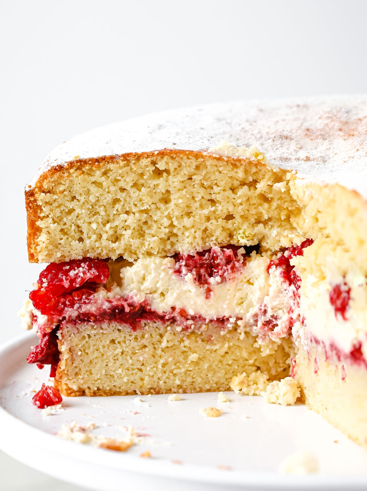 a sliced open almond flour sponge cake filled with raspberry jam, whipped cream and fresh raspberries