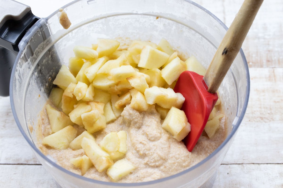 muffin batter and chopped apple in a food processor bowl with a spatula