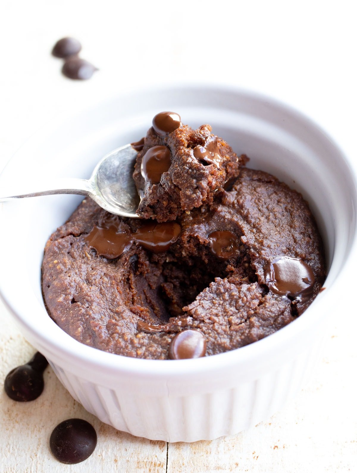 a spoonful of brownie resting on a ramekin with a mug brownie
