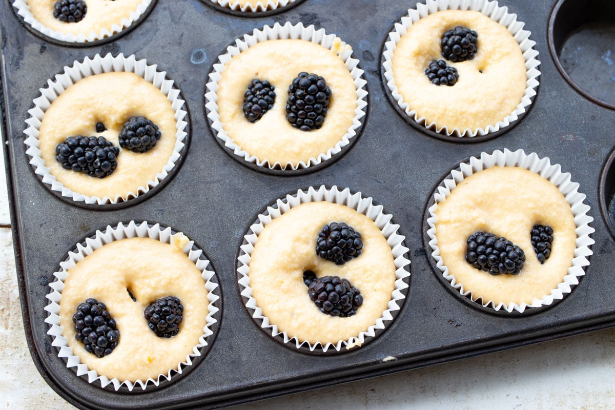 muffin batter with blackberries in paper cases